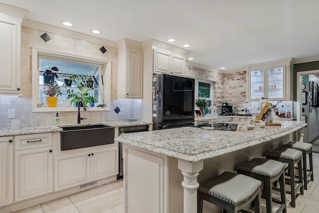 kitchen featuring light stone counters, black refrigerator, decorative backsplash, sink, and a kitchen island