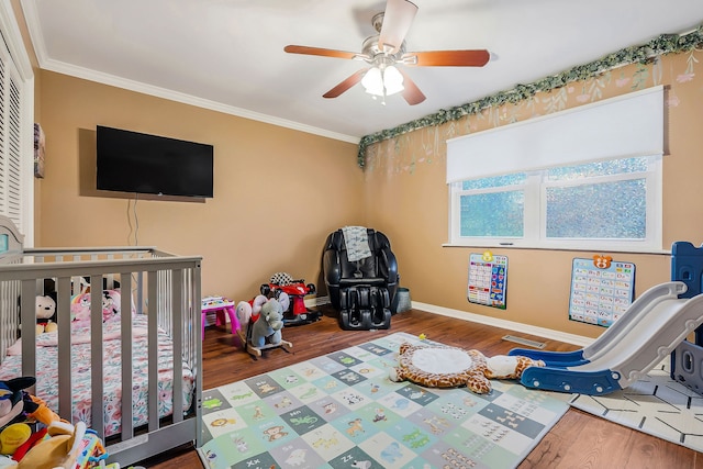 bedroom with a crib, ceiling fan, ornamental molding, and wood-type flooring