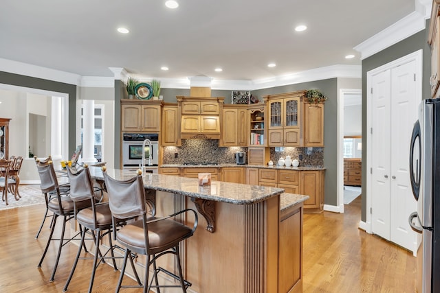 kitchen featuring crown molding, stainless steel appliances, light stone countertops, light hardwood / wood-style floors, and a center island