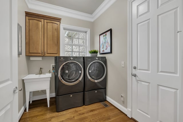 washroom featuring cabinets, light hardwood / wood-style floors, washing machine and dryer, and ornamental molding