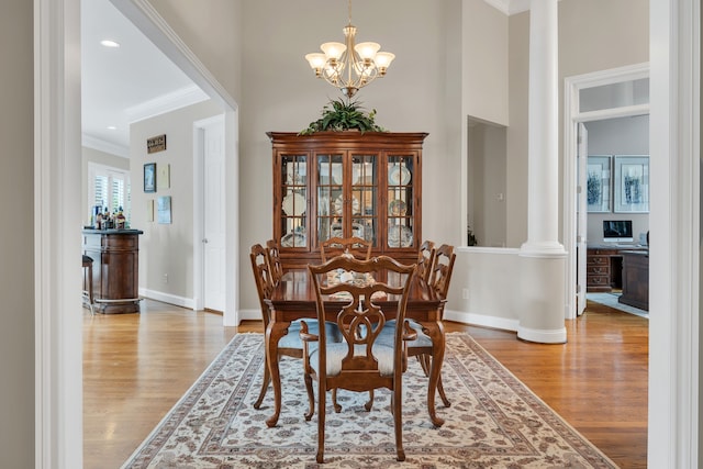 dining space featuring ornate columns, light wood-type flooring, crown molding, and a notable chandelier