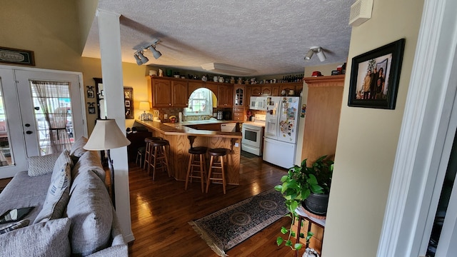 kitchen with kitchen peninsula, a textured ceiling, a kitchen breakfast bar, dark hardwood / wood-style floors, and white appliances