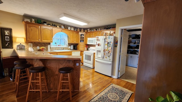 kitchen with kitchen peninsula, a breakfast bar area, white appliances, light wood-type flooring, and decorative backsplash