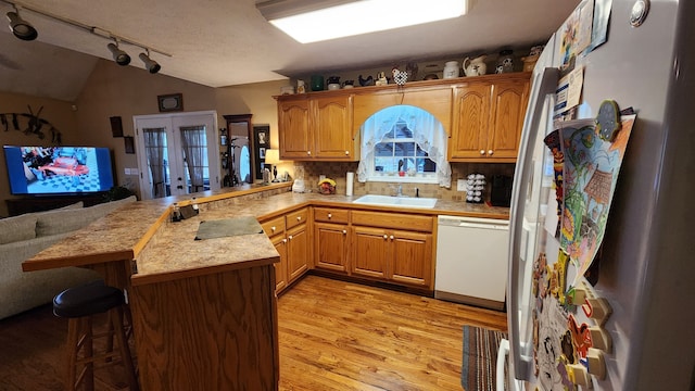 kitchen with white dishwasher, kitchen peninsula, sink, a kitchen breakfast bar, and backsplash