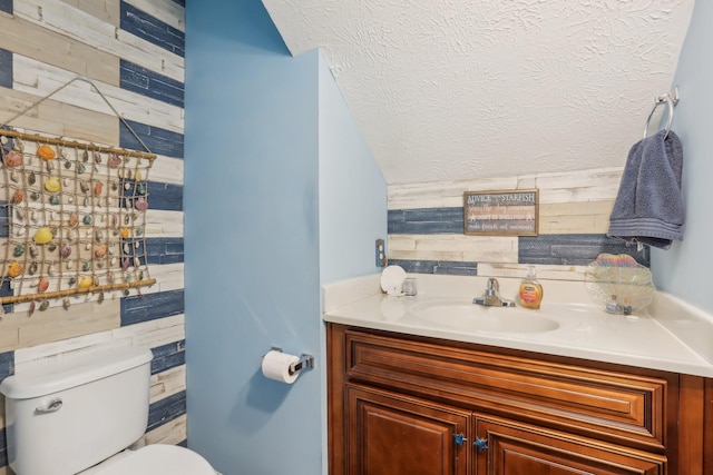 bathroom with a textured ceiling, vanity, toilet, and tile walls