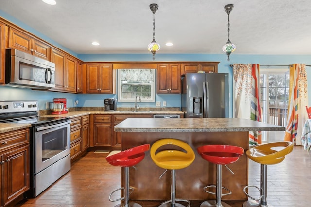 kitchen with stainless steel appliances, a kitchen island, hanging light fixtures, and sink