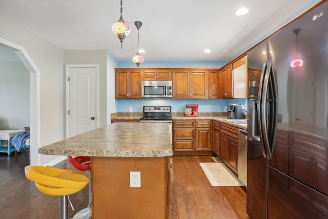 kitchen featuring a center island, hanging light fixtures, stainless steel appliances, wood-type flooring, and a kitchen bar