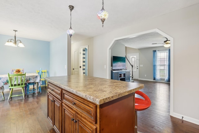 kitchen featuring dark hardwood / wood-style floors, a kitchen island, ceiling fan with notable chandelier, and decorative light fixtures