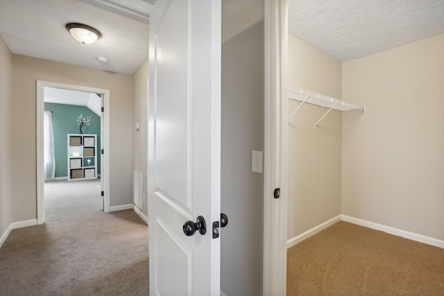 hall with a textured ceiling, light colored carpet, and lofted ceiling