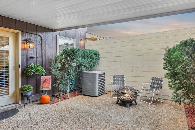 patio terrace at dusk featuring central air condition unit and a fire pit