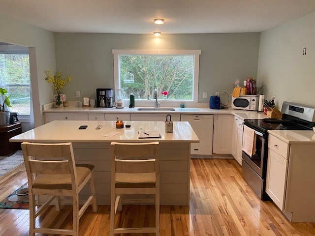 kitchen with white appliances, a breakfast bar area, light wood-type flooring, and a wealth of natural light