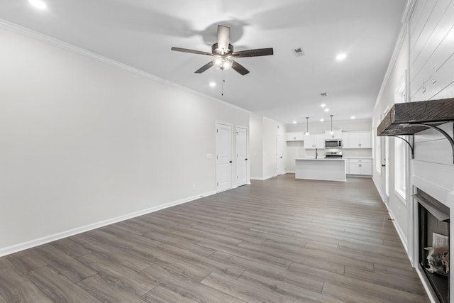 unfurnished living room featuring ceiling fan, hardwood / wood-style floors, and ornamental molding