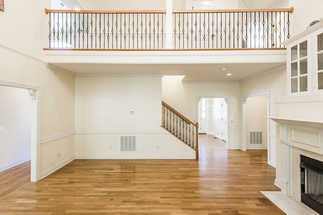 unfurnished living room with a towering ceiling, light hardwood / wood-style floors, and crown molding