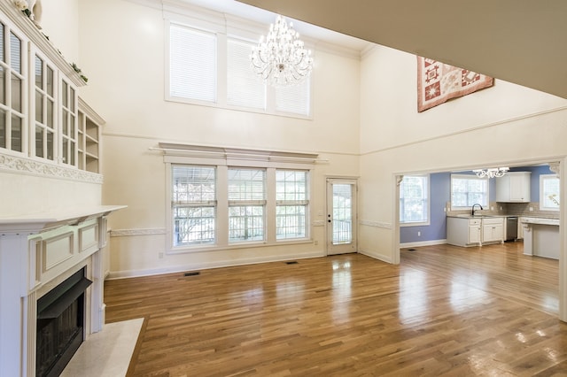 unfurnished living room with hardwood / wood-style floors, a towering ceiling, a chandelier, and sink