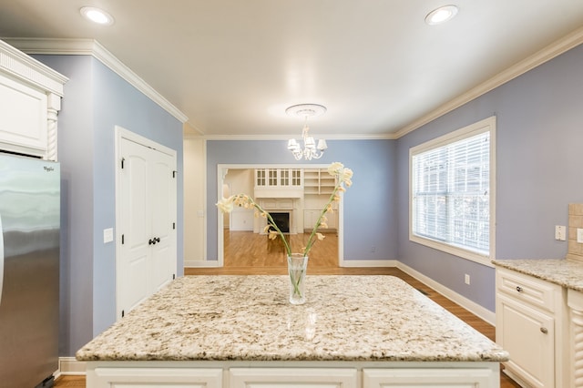 kitchen with light stone countertops, light hardwood / wood-style flooring, hanging light fixtures, and stainless steel fridge