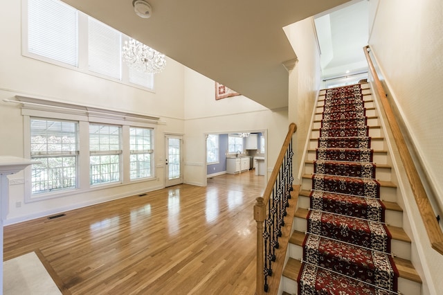 staircase with a high ceiling, an inviting chandelier, wood-type flooring, and plenty of natural light