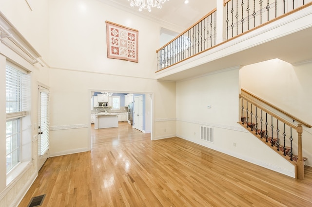 unfurnished living room with ornamental molding, a towering ceiling, light hardwood / wood-style flooring, and a chandelier