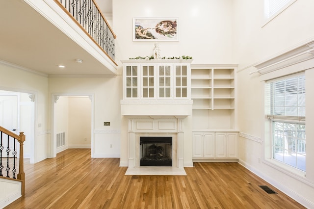 unfurnished living room with light wood-type flooring, a wealth of natural light, ornamental molding, and a towering ceiling