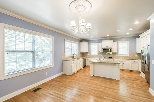 kitchen with appliances with stainless steel finishes, decorative light fixtures, a healthy amount of sunlight, and a center island