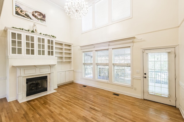 unfurnished living room featuring light hardwood / wood-style floors, a high ceiling, an inviting chandelier, and crown molding