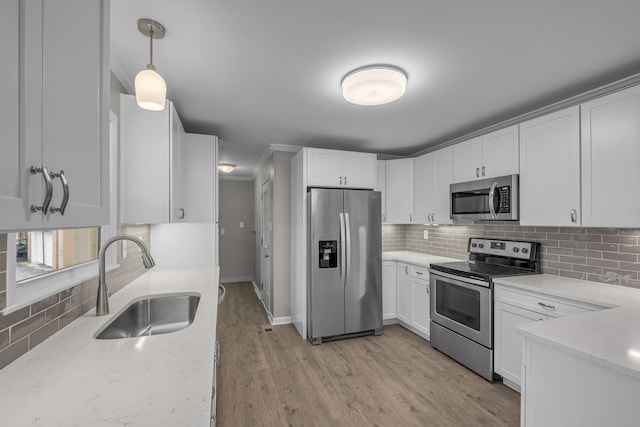 kitchen with stainless steel appliances, white cabinets, hanging light fixtures, sink, and light wood-type flooring