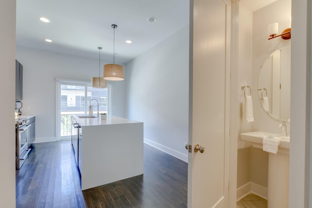 kitchen with hanging light fixtures, sink, a kitchen island with sink, stainless steel stove, and dark hardwood / wood-style floors