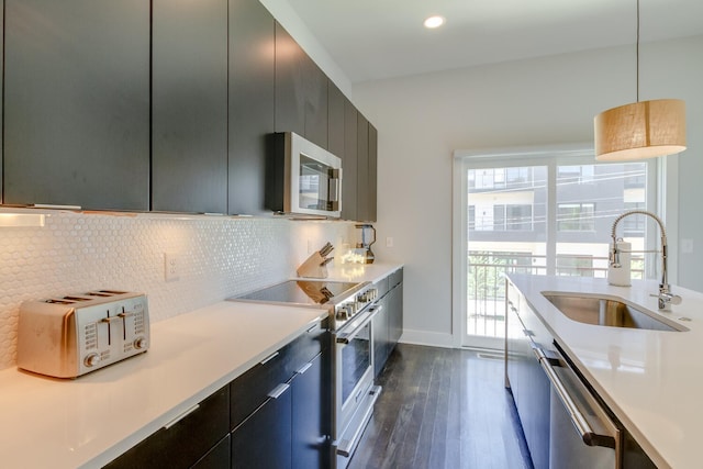 kitchen featuring stainless steel appliances, dark wood-type flooring, sink, backsplash, and decorative light fixtures