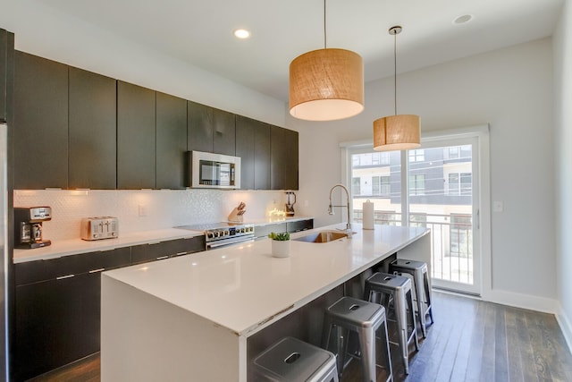 kitchen featuring a kitchen island with sink, appliances with stainless steel finishes, hanging light fixtures, and sink