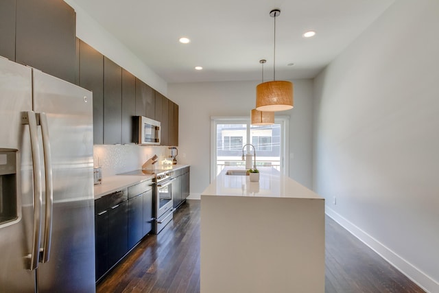 kitchen featuring sink, appliances with stainless steel finishes, dark hardwood / wood-style floors, hanging light fixtures, and a kitchen island with sink