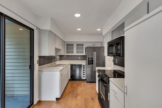 kitchen with black appliances, white cabinetry, sink, and light hardwood / wood-style floors