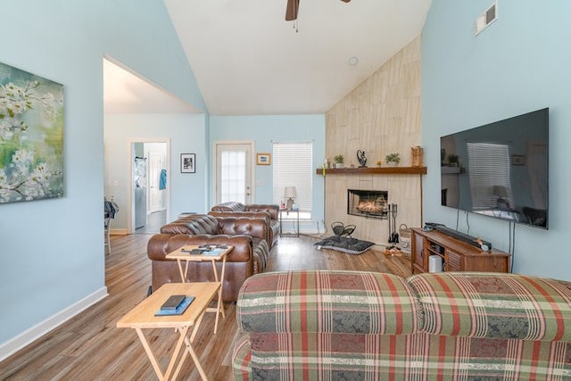 living room with high vaulted ceiling, light hardwood / wood-style flooring, ceiling fan, and a tile fireplace