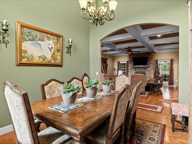 dining area with ceiling fan with notable chandelier, beam ceiling, a large fireplace, hardwood / wood-style floors, and coffered ceiling