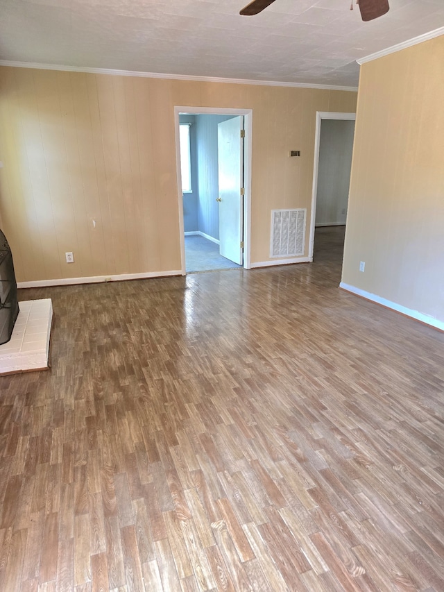 unfurnished living room with crown molding, wood-type flooring, ceiling fan, and a wood stove