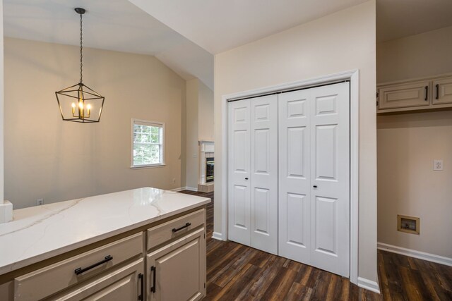 kitchen featuring dark hardwood / wood-style flooring, lofted ceiling, light stone counters, hanging light fixtures, and a notable chandelier