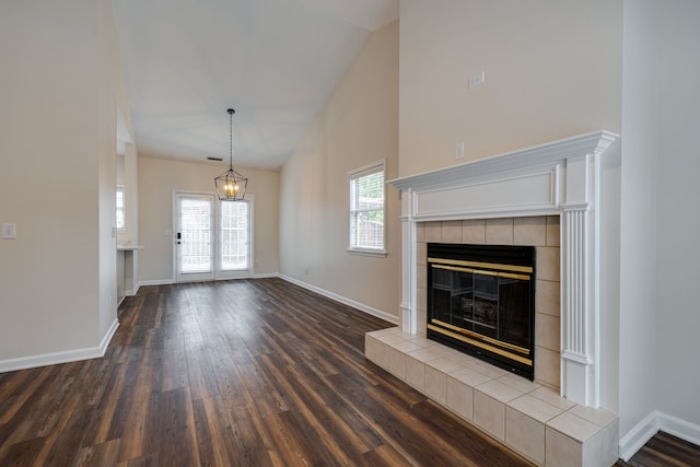 unfurnished living room with dark wood-type flooring, a healthy amount of sunlight, a tile fireplace, and high vaulted ceiling