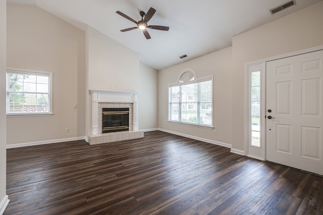 unfurnished living room with ceiling fan, a healthy amount of sunlight, a tiled fireplace, and dark hardwood / wood-style flooring