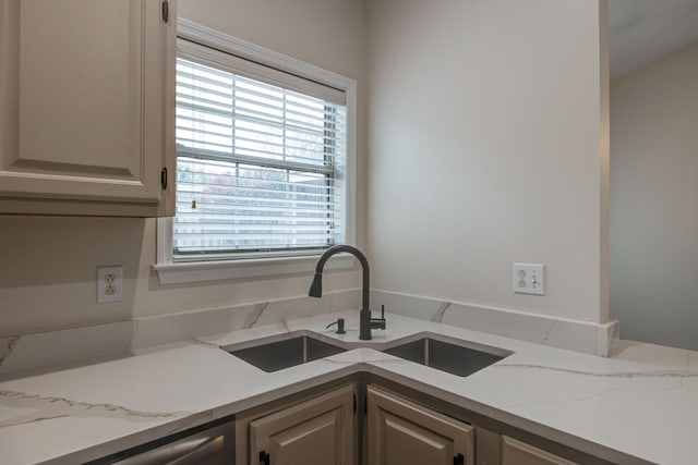 kitchen with stainless steel dishwasher, sink, and light stone counters