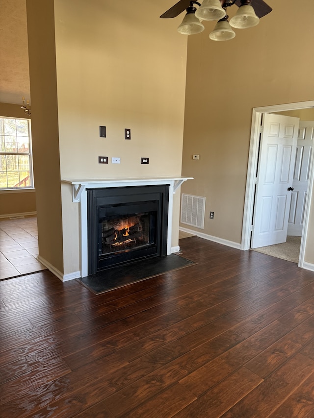 unfurnished living room with dark wood-type flooring, ceiling fan, and a high ceiling