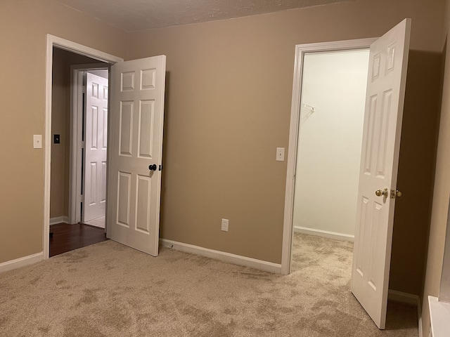 unfurnished bedroom with a spacious closet, light colored carpet, a textured ceiling, and a closet