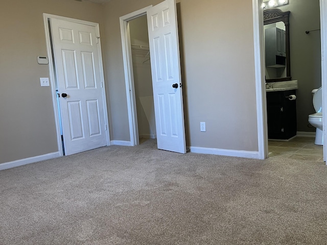 unfurnished bedroom with a walk in closet, connected bathroom, light carpet, and a closet