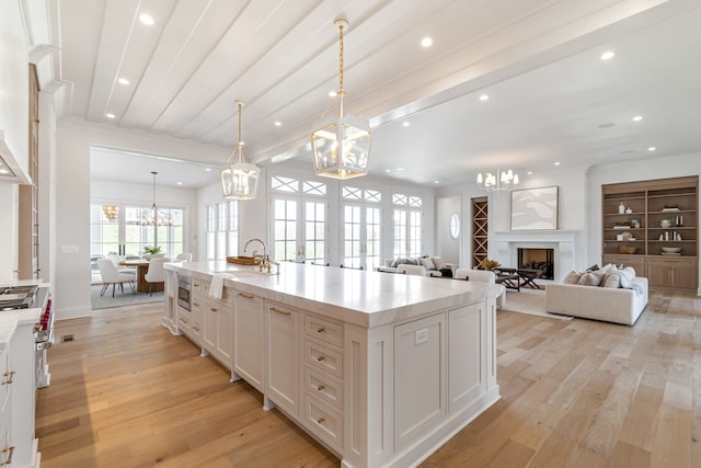 kitchen with an island with sink, open floor plan, hanging light fixtures, light countertops, and white cabinetry