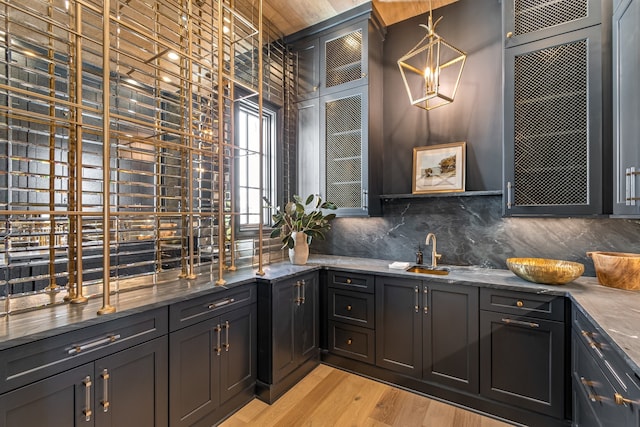 bar with light wood-type flooring, a sink, decorative light fixtures, and decorative backsplash