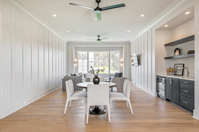 dining space featuring beverage cooler, ceiling fan, crown molding, light wood-style floors, and a decorative wall