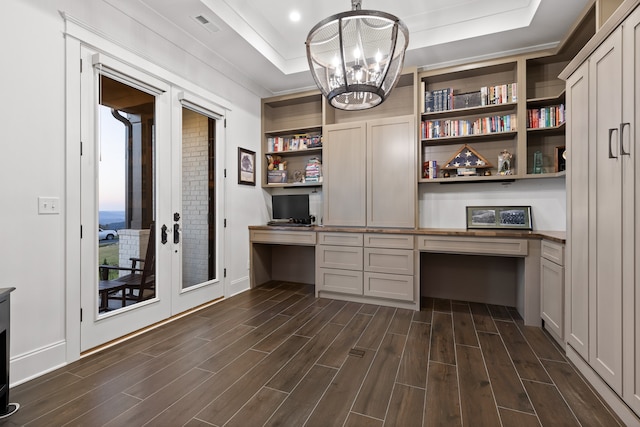 unfurnished office with built in desk, a raised ceiling, dark hardwood / wood-style flooring, and a notable chandelier