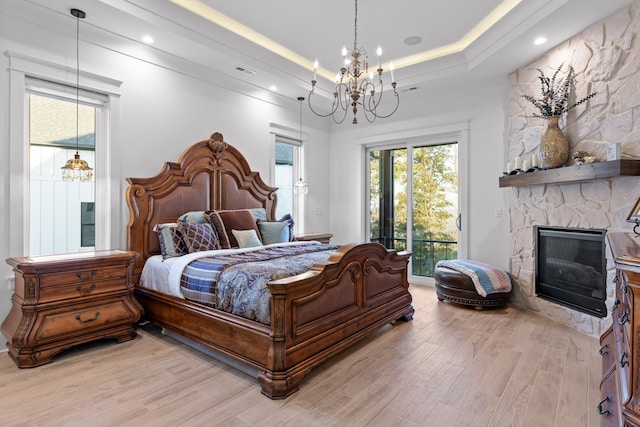 bedroom featuring light hardwood / wood-style floors, a tray ceiling, a fireplace, a chandelier, and access to outside