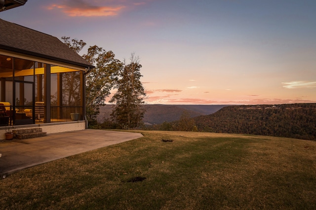 yard at dusk featuring a mountain view, a sunroom, and a patio area