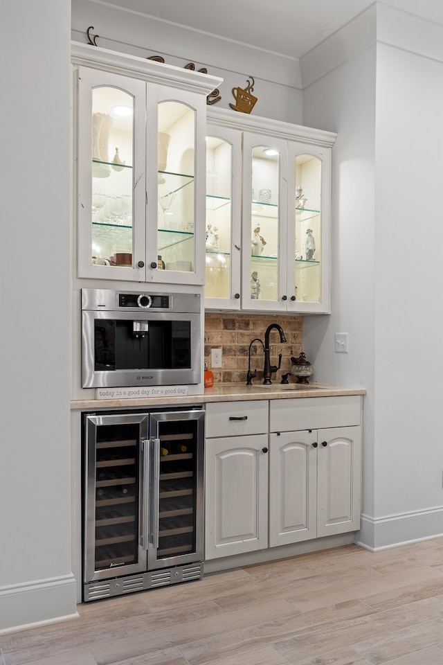 bar with stainless steel oven, white cabinetry, sink, beverage cooler, and light hardwood / wood-style flooring