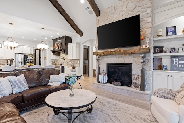 living room featuring a stone fireplace, light wood-type flooring, and lofted ceiling with beams