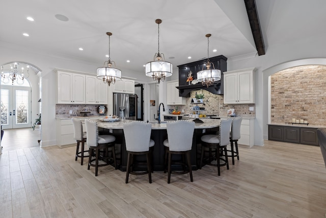 kitchen featuring a large island with sink, beam ceiling, stainless steel refrigerator with ice dispenser, hanging light fixtures, and white cabinets