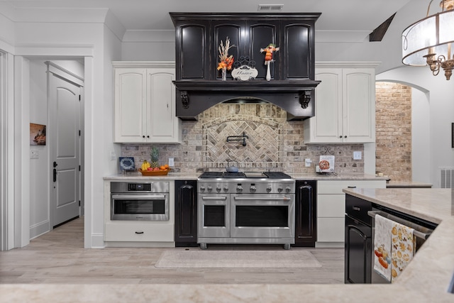 kitchen featuring tasteful backsplash, appliances with stainless steel finishes, custom range hood, and light hardwood / wood-style flooring